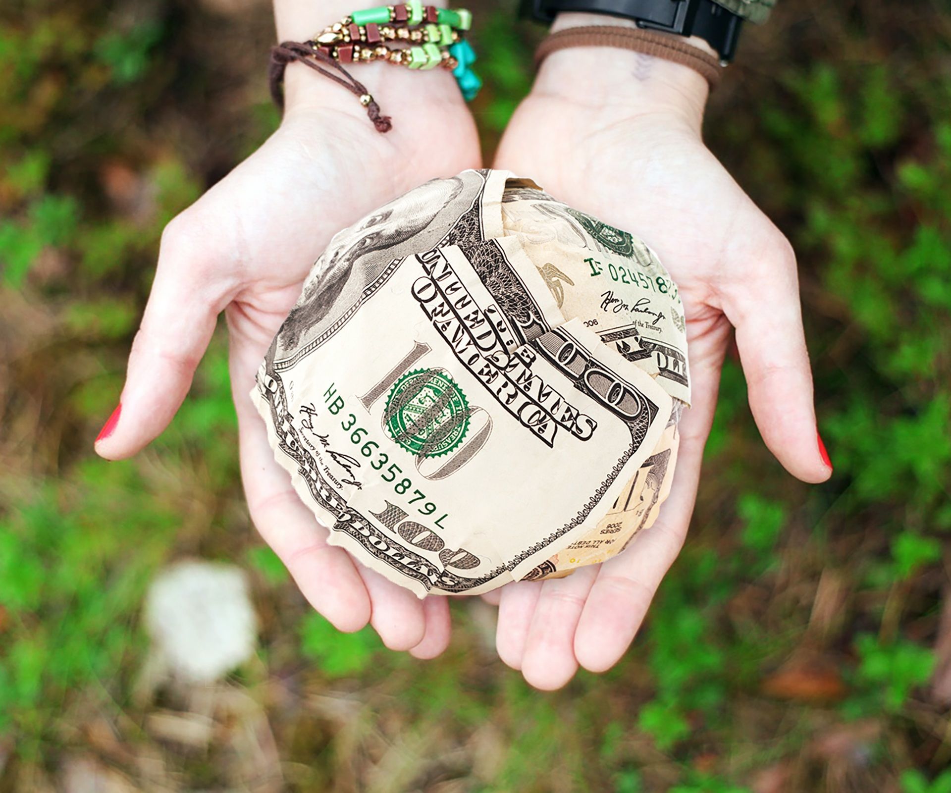 Hands holding crumpled money outdoors, symbolizing cash transfers and financial support