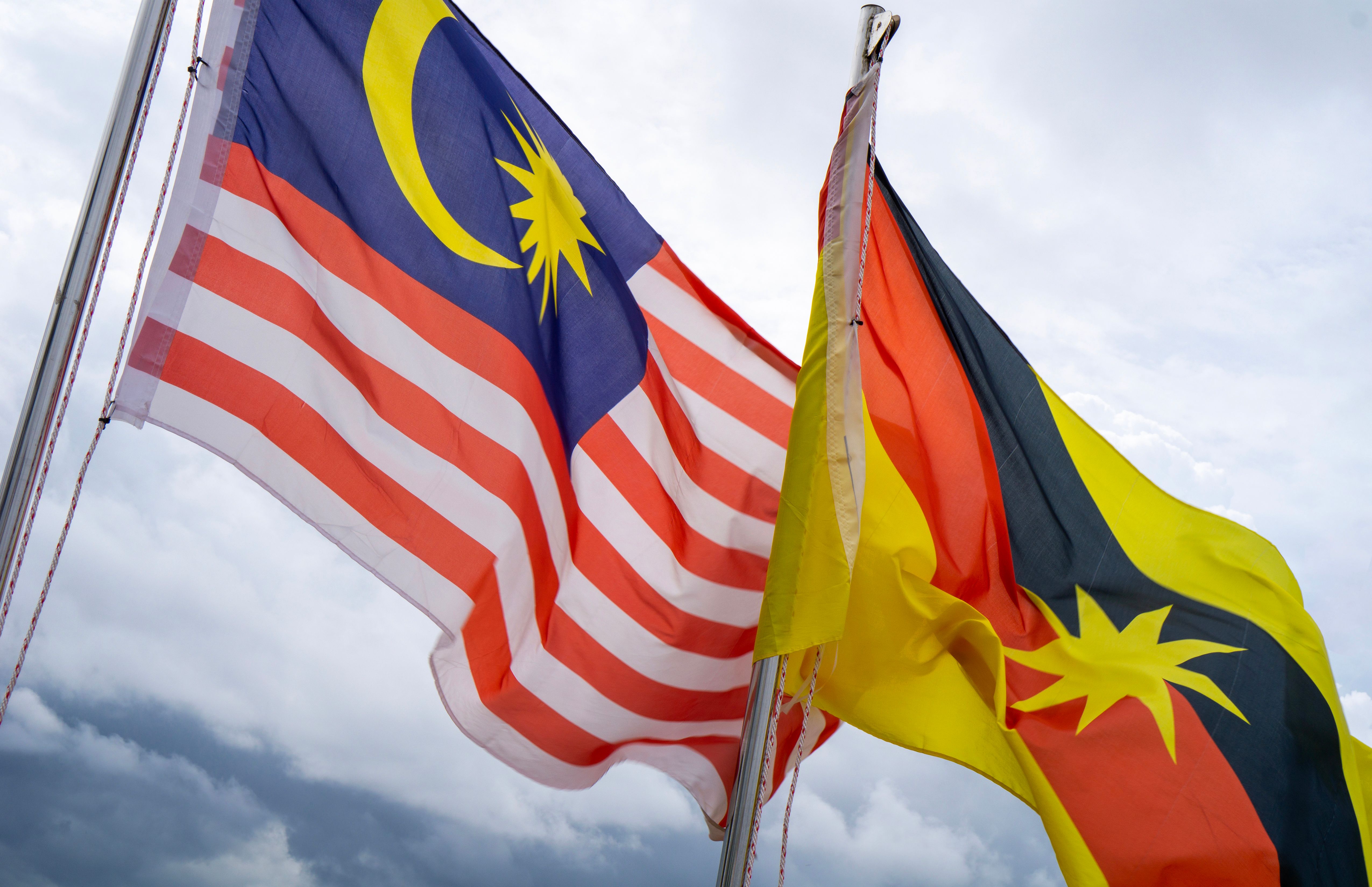 Malaysian and Sarawakian flags waving together under a cloudy sky