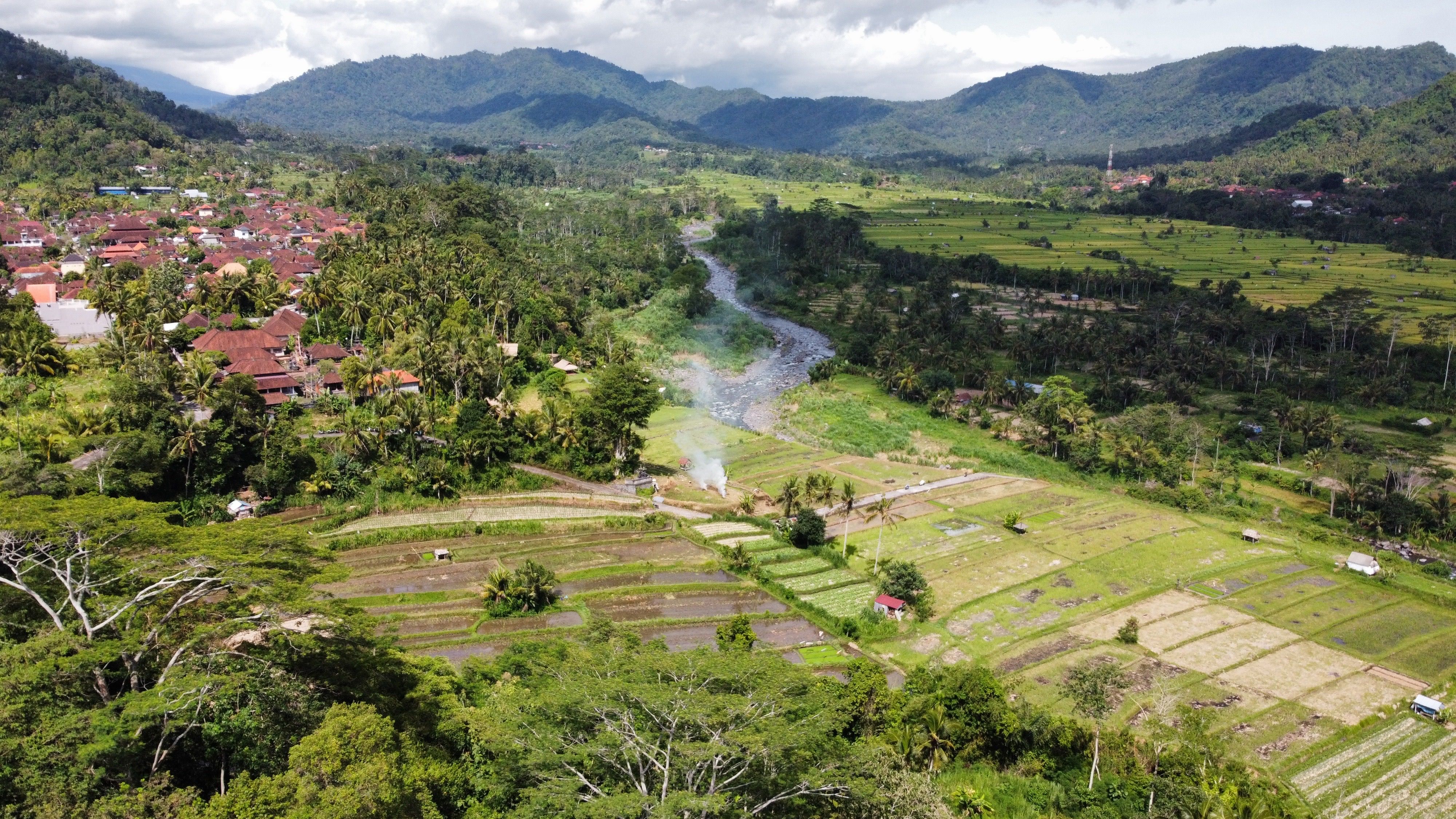 Aerial view of lush rural countryside with river, fields, forest and village clusters in Southeast Asia